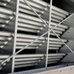 a close-up image of a large industrial air conditioning or cooling unit with metal fins and protective grilles, typically found on the exterior of a commercial building.
