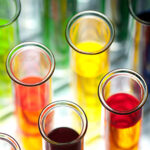 A collection of test tubes filled with brightly colored liquids, arranged in a rack with a blurred background.