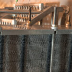 a close-up of industrial equipment featuring a dense network of metal fins or coils, likely part of a heat exchanger or cooling unit, with various pipes and fixtures connected to it.
