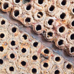 a close-up of a corroded metal surface with numerous rusted holes and deposits, which may be a part of industrial machinery or infrastructure showing signs of significant wear and decay.