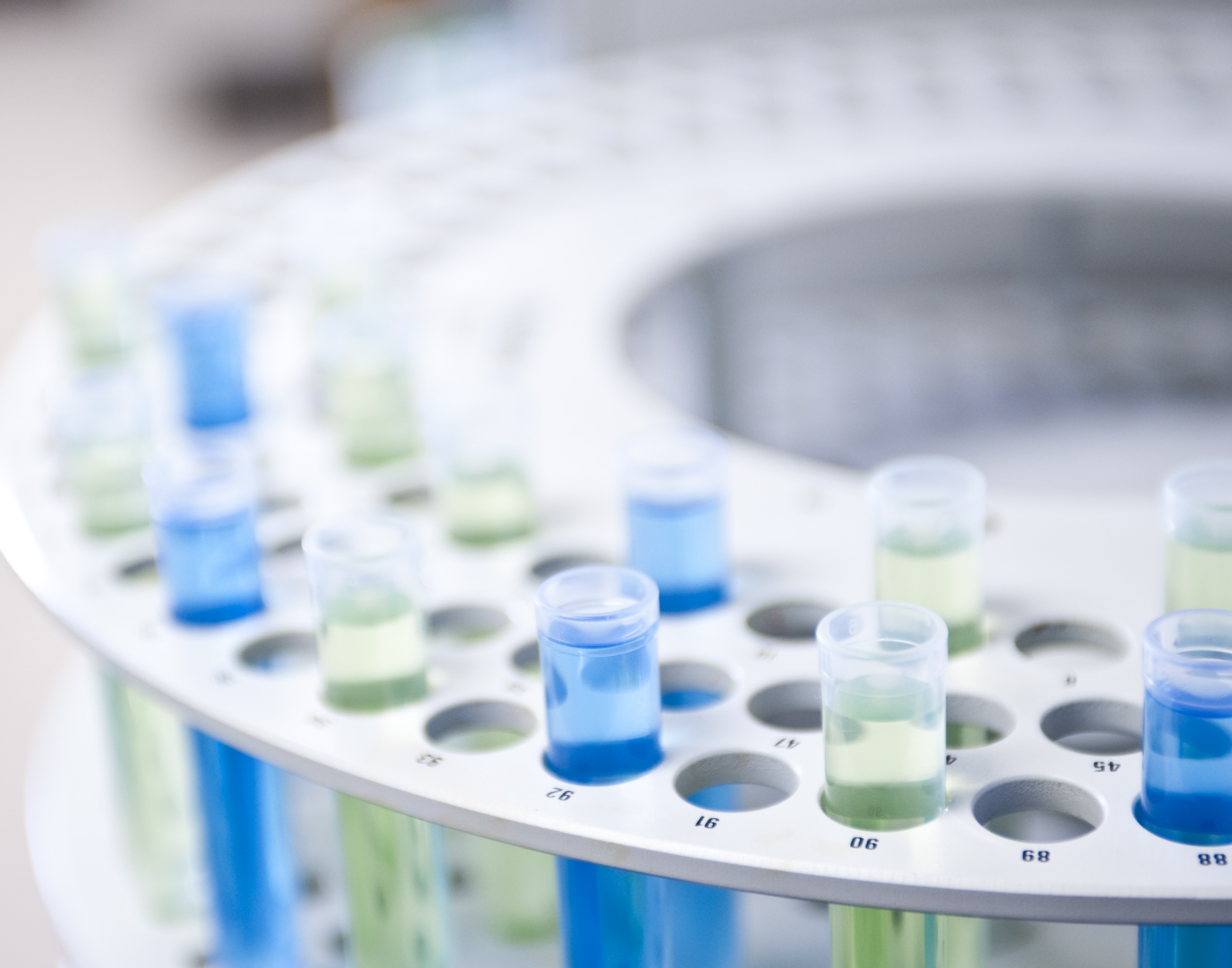 A close-up of test tubes with blue and green liquids in a circular holder, suggesting a scientific experiment or analysis.