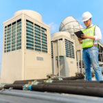 Engineer holding tablet is checking the cooling tower on the roof of the building to be in good condition.