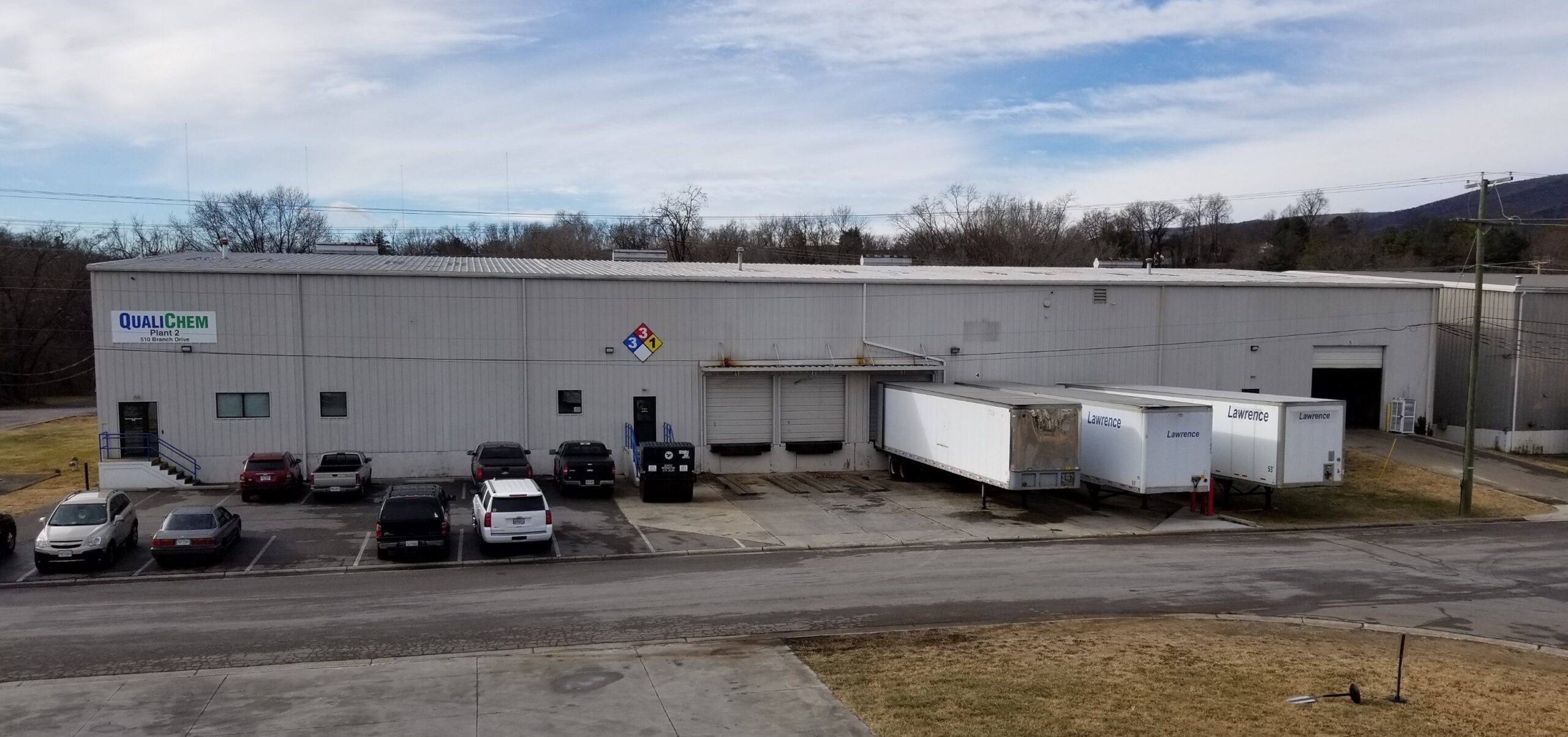 An exterior view of the plant 2 QualiChem building with a parking lot in front and several trailers docked at the loading area.
